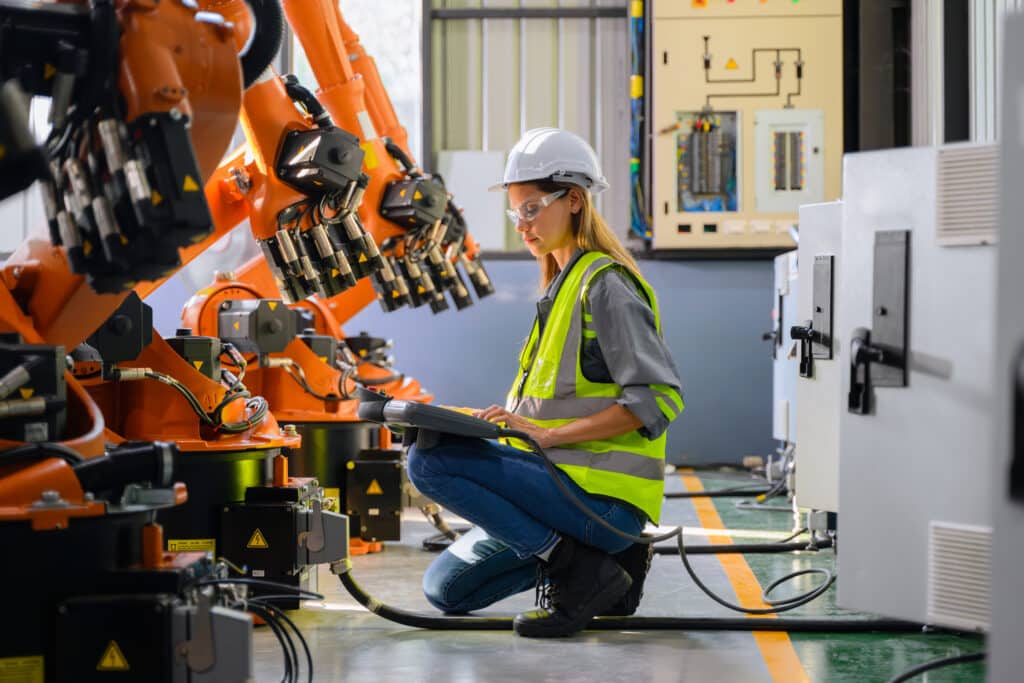 Weibliche Ingenieurin, die in einer Fabrik mit einer automatisierten Robotermaschine arbeitet, weiblicher Techniker mit intelligenter Technologie in der Industrie, weiblicher Arbeiter, der Teile einer Robotermaschine überprüft und kontrolliert